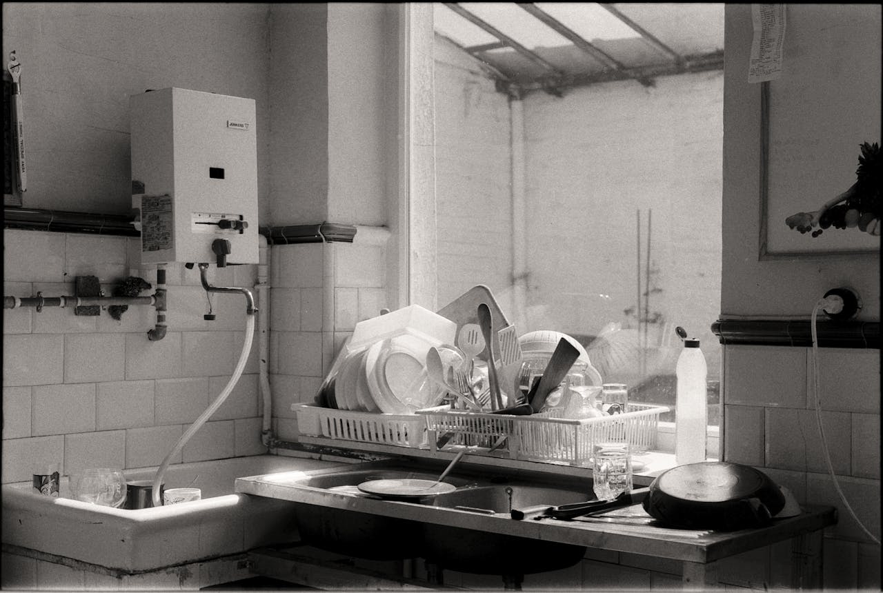 digital Black and white image of a kitchen sink filled with dishes and cutlery by the window.