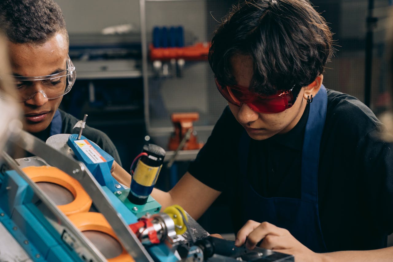 Services-01 Two young engineers concentrating on precision work in a technical workshop, wearing safety goggles.